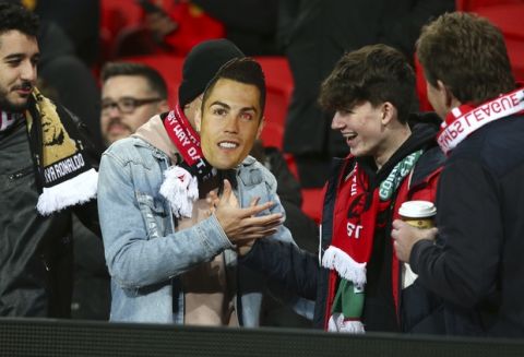 A Manchester United fan shakes hands with another one wearing a Juventus forward Cristiano Ronaldo mask on the stands before the Champions League group H soccer match between Manchester United and Juventus at Old Trafford, Manchester, England, Tuesday, Oct. 23, 2018. (AP Photo/Dave Thompson)