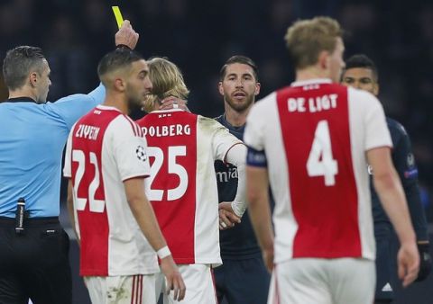 This Wednesday Feb. 13, 2019, image shows referee Damir Skomina, left, showing a yellow card to Real's Sergio Ramos, center, after a foul on Ajax's Kasper Dolberg during the first leg, round of sixteen, Champions League soccer match between Ajax and Real Madrid at the Johan Cruyff ArenA in Amsterdam, Netherlands. UEFA is investigating reported comments by Real Madrid captain Sergio Ramos that he intentionally got a yellow card to provoke a favorable Champions League ban. (AP Photo/Peter Dejong)