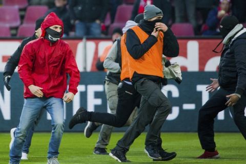 Masked Cologne fans including one dressed as a steward, center,  running across the pitch with a flag stolen from Moenchengladbach fans during the German Bundesliga soccer  match between 1. FC Cologne and Borussia Moenchengladbach at the RheinEnergieStadion in Cologne, Germany, Sunday, Jan. 14, 2018.  (Rolf Vennenbernd/dpa via AP)