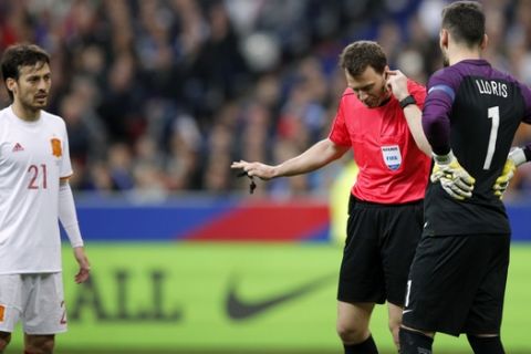 Spain's scorer David Silva, left, and France's goalkeeper Hugo Lloris, right, look on as Referee Felix Zwayer, center, from Germany holds his earphone during the international friendly soccer match between France and Spain at the Stade de France in Paris, France, Tuesday, March 28, 2017. The match saw the first use in France of video replays to help the referee, with the technology being used to confirm Deulofeu's goal and to disallow one for France's Antoine Griezmann just after halftime. (AP Photo/Christophe Ena)