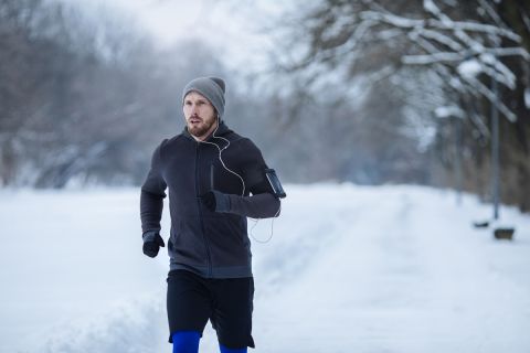 Young man running outdoors at winter listening to music