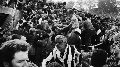 A crowd of soccer fans in the Brussels Heysel stadium, falls down in a heavy group over the broken fence just prior to the European Champions Cup Final between Liverpool and Juventus of Turin, Italy, May 29, 1985. The incident that caused many deaths and injured occurred after riots in the stands between the various soccer fan groups. (AP Photo/Gianni Foggia)