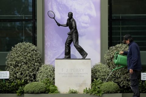 A gardener waters the plants alongside a statue of former Wimbledon Champion Fred Perry at the All England Lawn Tennis Club in Wimbledon in London, Monday, June 29, 2020.  The 2020 Wimbledon Tennis Championships, that were due to start today but have been cancelled due to the Coronavirus pandemic. (AP Photo/Kirsty Wigglesworth)