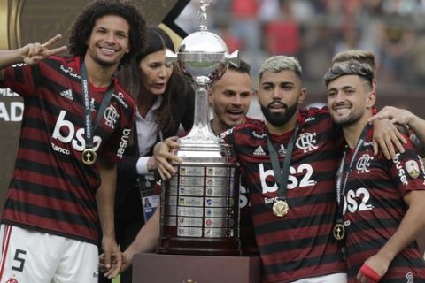 Willian Arao, left, Gabriel, second from right, and Arrascaeta of Brazil's Flamengo, right, celebrate with the trophy after his team defeated Argentina's River Plate 2-1 to win the the Copa Libertadores final soccer match at the Monumental stadium in Lima, Peru, Saturday, Nov. 23, 2019. (AP Photo/Martin Mejia)