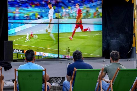 People sit in an outdoor restaurant and watch the Euro 2020 opening game between Turkey and Italy in Frankfurt, Germany, Friday, June 11, 2021. (AP Photo/Michael Probst)