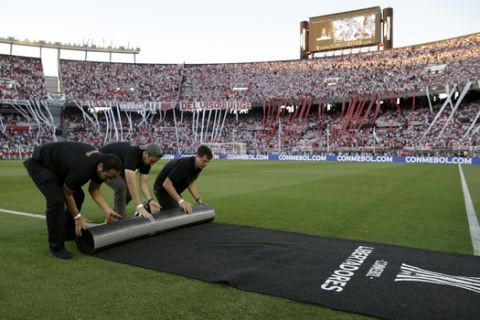 Workers remove a carpet from the field after the final soccer match of the Copa Libertadores was rescheduled for Sunday, at the Antonio Vespucio Liberti stadium in Buenos Aires, Argentina, Saturday, Nov. 24, 2018. South American soccer body CONMEBOL has postponed the Copa Libertadores final to Sunday after Boca Juniors bus was attacked by River Plate fans. (AP Photo/Ricardo Mazalan)