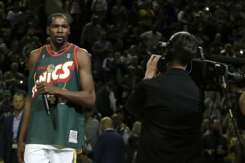 Golden State Warriors forward Kevin Durant addresses the crowd, while wearing the jersey of Seattle SuperSonics legend Shawn Kemp before an NBA basketball preseason game against the Sacramento Kings, Friday, Oct. 5, 2018, in Seattle. (AP Photo/Ted S. Warren)