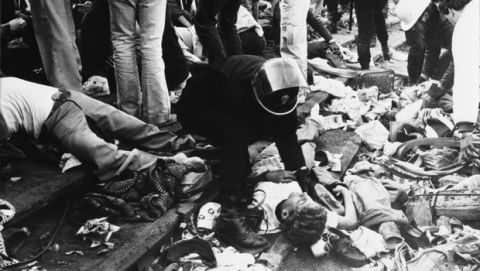 EDS: NOTE GRAPHIC CONTENT: FILE - In this May 29, 1985 file photo, a Belgian riot policeman kneels over bodies lying on the ground inside the Heysel soccer stadium in Brussels. Local authorities, families of victims and survivors marked the 30th anniversary of the Heysel stadium tragedy Friday, May 29, 2015 to commemorate the 39 football fans who died during hooligan riots at the 1985 European Cup final between Liverpool and Juventus. (AP Photo/Gianni Foggia, File)