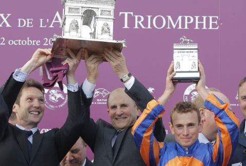 Irish Ryan-Lee Moore, left, and Irish horse owner Mikel Tabor, center, and a unidentified staff member hold their trophies on the podium of the Qatar Prix de l'Arc de Triomphe horse race at the Chantilly horse racetrack, 40 kms(25 miles) north of  Paris, France, Sunday, Oct. 2, 2016. (AP Photo/Michel Euler)