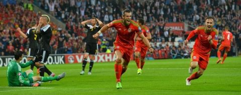Wales's midfielder Gareth Bale (C) celebrates scoring the opening goal with Wales's midfielder Aaron Ramsey (R) as Belgium's goalkeeper Thibaut Courtois (L) and Belgium's midfielder Radja Nainggolan (2L) react during the Euro 2016 qualifying group B football match between Wales and Belgium at Cardiff City Stadium in Cardiff, south Wales, on June 12, 2015.  AFP PHOTO / GLYN KIRK        (Photo credit should read GLYN KIRK/AFP/Getty Images)