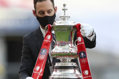 The trophy is handled by a man wearing a face mask after the FA Cup final soccer match between Arsenal and Chelsea at Wembley stadium in London, England, Saturday, Aug.1, 2020. (Catherine Ivill/Pool via AP)