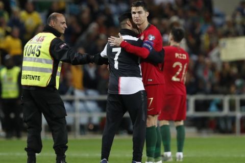 A supporter, who jumped into the pitch, is taken away after taking a selfie with Portugal's Cristiano Ronaldo, right, during the Euro 2020 group B qualifying soccer match between Portugal and Lithuania at the Algarve stadium outside Faro, Portugal, Thursday, Nov. 14, 2019. (AP Photo/Armando Franca)