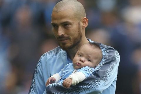 Manchester City's David Silva carries a child believed to be his son during the English Premier League soccer match between Manchester City and Huddersfield Town at the Etihad Stadium in Manchester, England, Sunday, Aug. 19, 2018. (AP Photo/Dave Thompson)