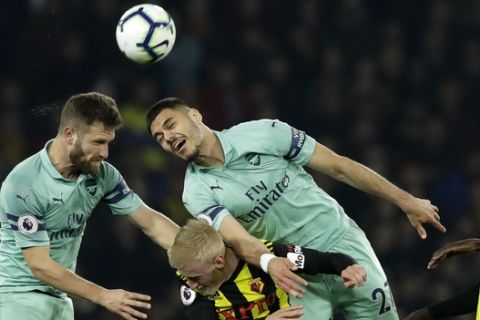 Arsenal's Shkodran Mustafi, left, and Konstantinos Mavropanos jump for the ball above Watford's Will Hughes as Watford's Abdoulaye Doucoure, right, looks on during the English Premier League soccer match between Watford and Arsenal at Vicarage Road stadium in Watford, England, Monday, April 15, 2019. (AP Photo/Matt Dunham)