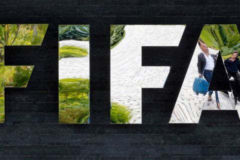 FILE - In this May 27, 2015, file photo, two persons are reflected in the FIFA logo at the FIFA headquarters in Zurich, Switzerland. Swiss authorities said Thursday, July 16, 2015, that one of the seven FIFA officials arrested in Zurich as part of a U.S. corruption probe was extradited to the United States they day before. Switzerland's Federal Office of Justice didn't identify the FIFA official.  (AP Photo/Michael Probst, File)