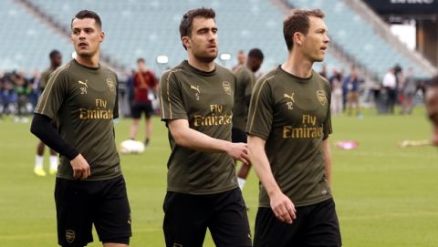 Arsenal's Granit Xhaka, Sokratis Papastathopoulos and Stephan Lichtsteiner, from left to right, walk on the pitch during a soccer training session at the Olympic stadium in Baku, Azerbaijan, Tuesday May 28, 2019. English Premier League teams Arsenal and Chelsea are preparing for the Europa League Final soccer match that takes place in Baku on Wednesday night. (AP Photo/Darko Bandic)