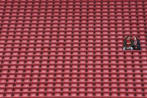 People sit surrounded by empty seats as they wait for the start of the English Premier League soccer match between Liverpool and Bournemouth at Anfield stadium in Liverpool, England, Saturday, March 7, 2020. (AP Photo/Jon Super)