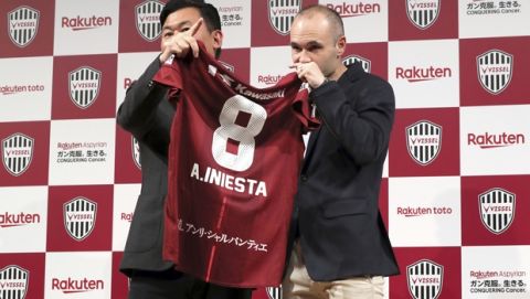 Former Barcelona player Andres Iniesta, right, holding his new uniform with Hiroshi Mikitani, left, owner of Vissel Kobe, prepare for a photo session during a press conference announcing Iniesta's move to Japan's Vissel Kobe in Tokyo Thursday, May 24, 2018. (AP Photo/Eugene Hoshiko)