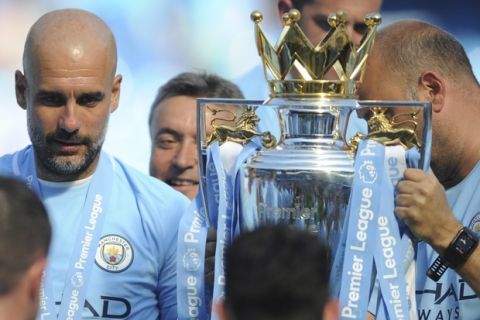 Manchester City manager Josep Guardiola, left, looks at the English Premier League trophy after the soccer match between Manchester City and Huddersfield Town at Etihad stadium in Manchester, England, Sunday, May 6, 2018. (AP Photo/Rui Vieira)