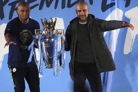 Manchester City coach Pep Guardiola, right, and captain Vincent Kompany hold the trophy as they celebrate with their supporters at the Etihad Stadium in Manchester, England, Sunday May 12, 2019 the day they won the English Premier League title. Manchester City retained the Premier League trophy after coming from behind to beat Brighton 4-1 and see off Liverpool's relentless challenge on the final day of the season on Sunday. (AP Photo/Jon Super)