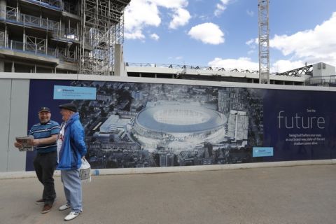 Football fans smile as they pass a poster showing the plans for the new stadium, in front of construction work at White Hart Lane stadium in London, Sunday, May 14, 2017. Later Sunday, Tottenham Hotspur will play Manchester United in an English Premier League soccer match, it will be the last Spurs match at the old stadium, a new stadium is being built on the site. (AP Photo/Frank Augstein)