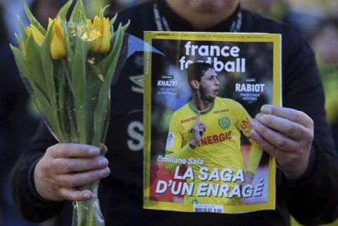 A FC Nantes soccer fan displays an old copy of French soccer magazine, France Football, featuring FC Nantes soccer player Emiliano Sala of Argentina, during a tribute in Nantes, western France, Tuesday, Jan. 22, 2019. The French civil aviation authority said Tuesday, Emiliano Sala was aboard a small passenger plane that went missing off the coast of the island of Guernsey. (AP Photo/David Vincent)