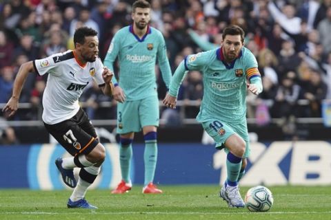 Barcelona's Lionel Messi, right, challenges for the ball with Valencia's Francis Coquelin during the Spanish La Liga soccer match between Valencia and Barcelona at the Mestalla Stadium in Valencia, Spain, Saturday, Jan. 25, 2020. (AP Photo/Alberto Saiz)