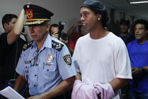 Former soccer star Ronaldinho talks as he walks escorted by Police officers with hands handcuffed to declare to judge Clara Ruiz Diaz at Justice Palace in Asuncion, Paraguay, Saturday, March 7, 2020. Ronaldinho and his brother Roberto de Assis Moreira, right back, were alleged to enter to the country with a false Paraguayan passport.(AP Photo/Jorge Saenz)