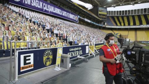 A TV cameraperson, wearing a protective mask against the spread of coronavirus, works in front of cardboards with photographs of Fenerbahce fans on the stands prior to a Turkish Super League soccer match between Fenerbahce and Kayserispor in Istanbul, Friday, June 12, 2020. The Turkish Super Lig resumed its season on Friday without spectators after it had suspended games since March 20 due to the coronavirus pandemic, later than many other European leagues. (Erdem Sahin/Pool via AP)