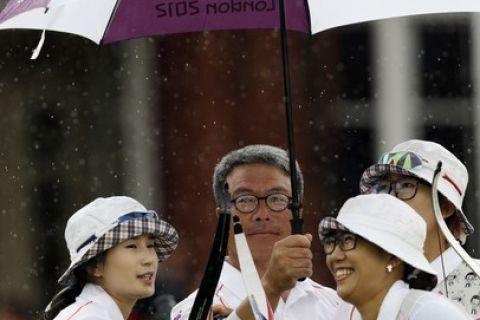 South Korea's team from left, Ki-bo bae, and unidentifed coach, Choi Hyeon-ju and Lee Sung-jin shield from the rain during the women's archery team competition at the 2012 Summer Olympics, Sunday, July 29, 2012, in London. (AP Photo/Marcio Jose Sanchez)