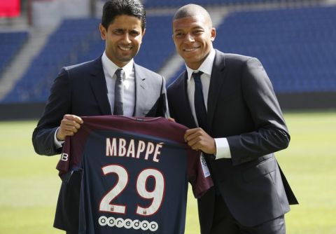 French soccer player Kylian Mbappe, right, and chairman of Paris Saint-Germain Nasser Al-Khelaifi pose with his team shirt following a press conference in Paris, Wednesday, Sept. 6, 2017. Mbappe is a young man in a big hurry and wants to "win everything" with his new club Paris Saint-Germain. (AP Photo/Christophe Ena)