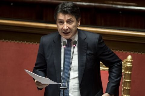 Italian Premier Giuseppe Conte adjusts his jacket as he refers to parliament on the ongoing Covid-19 situation, in Rome, Thursday, March 26, 2020. After more than two weeks of a nationwide lockdown to halt the spread of the coronavirus, the Italian government decided to expand the mandatory closure of nonessential commercial activities to heavy industry in the eurozone's third-largest economy, a major exporter of machinery, textiles and other goods. The new coronavirus causes mild or moderate symptoms for most people, but for some, especially older adults and people with existing health problems, it can cause more severe illness or death.  (Roberto Monaldo/LaPresse via AP)