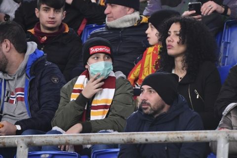 An AS Roma fan wears a sanitary mask as he watches the Italian Serie A soccer match between Roma and Lecce at the Olympic stadium in Rome, Sunday, Feb. 23, 2020. Four Serie A matches were postponed in Northern Italy for concern on possible spreading of the COVID-19 viral illness. (Alfredo Falcone/LaPresse via AP)
