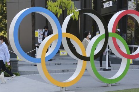 A woman with her dog walks past the Olympic rings in Tokyo, Tuesday, April 20, 2021.