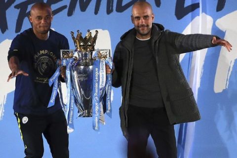 Manchester City coach Pep Guardiola, right, and captain Vincent Kompany hold the trophy as they celebrate with their supporters at the Etihad Stadium in Manchester, England, Sunday May 12, 2019 the day they won the English Premier League title. Manchester City retained the Premier League trophy after coming from behind to beat Brighton 4-1 and see off Liverpool's relentless challenge on the final day of the season on Sunday. (AP Photo/Jon Super)