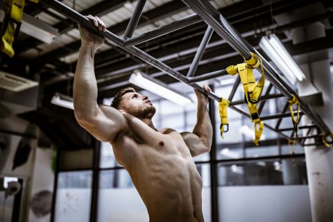 Young muscular build athlete exercising chin-ups in a gym.