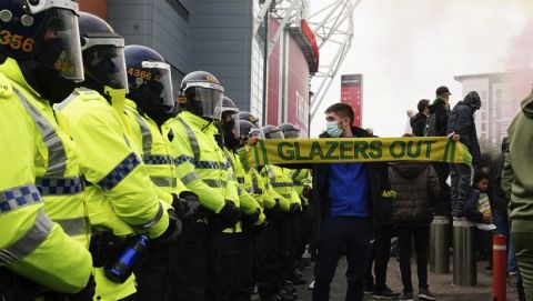 A Manchester United fan holds a protest scarf up next to a line of police during a protest against the Glazer family, the American owners of Manchester United, before their English Premier League soccer match against Liverpool at Old Trafford stadium in Manchester, England, Thursday, May 13, 2021. (AP Photo/Jon Super)