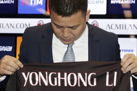 Chinese businessman Yonghong Li looks down to his name on an AC Milan jersey, during a press conference to illustrate takeover of AC Milan soccer club by a Chinese consortium, in Milan, Italy, Friday, April 14, 2017. A new era began at AC Milan on Thursday after the sale of Italy's most successful club to a Chinese-led consortium ended Silvio Berlusconi's 31 years in charge. (AP Photo/Antonio Calanni)
