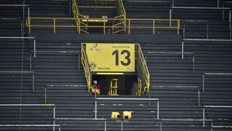 A steward watches from the empty stands as players exercise during warmup before the German Bundesliga soccer match between Borussia Dortmund and Schalke 04 in Dortmund, Germany, Saturday, May 16, 2020. The German Bundesliga becomes the world's first major soccer league to resume after a two-month suspension because of the coronavirus pandemic. (AP Photo/Martin Meissner, Pool)