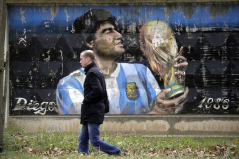 A man walks past a fence with graffiti depicting Argentina's soccer legend Diego Maradona in the town of Volkhov, 130 km (80 miles) east of St.Petersburg, Russia, Monday, Oct. 2, 2017. (AP Photo/Dmitri Lovetsky)