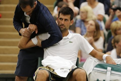 Serbia's Novak Djokovic receives treatment from a trainer during a break in his Men's Singles Match against Adrian Mannarino of France on day eight at the Wimbledon Tennis Championships in London Tuesday, July 11, 2017. (AP Photo/Alastair Grant)