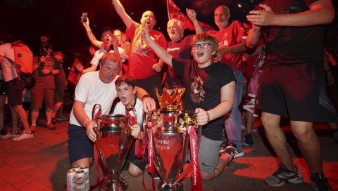 Liverpool supporters with replica Premier League and Champions League trophies as they celebrate outside of Anfield Stadium in Liverpool, England, Thursday, June 25, 2020 after Liverpool clinched the English Premier League title. Liverpool took the title after Manchester City failed to beat Chelsea on Wednesday evening. (AP photo/Jon Super)