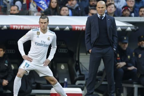 Real Madrid's Gareth Bale stretches next to Real Madrid's head coach Zinedine Zidane while waiting to come on as substitute during a Spanish La Liga soccer match between Real Madrid and Barcelona at the Santiago Bernabeu stadium in Madrid, Spain, Saturday, Dec. 23, 2017. (AP Photo/Paul White)