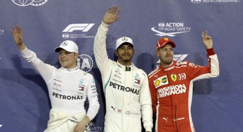 Mercedes driver Lewis Hamilton of Britain, center, who earned pole position, Ferrari driver Sebastian Vettel of Germany, right, who came in third and Mercedes driver Valtteri Bottas of Finland, left, who earned the second best time, posing for photos after the qualifying session for the Emirates Formula One Grand Prix at the Yas Marina racetrack in Abu Dhabi, United Arab Emirates, Saturday, Nov. 24, 2018. The Emirates Formula One Grand Prix will take place on Sunday. (AP Photo/Luca Bruno)