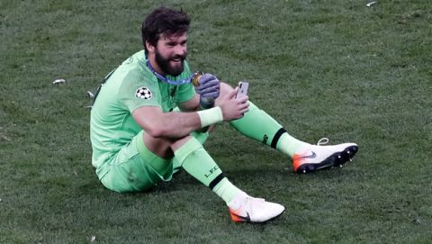 Liverpool goalkeeper Alisson shows medal to phone and smiles as he celebrates after winning the Champions League final soccer match between Tottenham Hotspur and Liverpool at the Wanda Metropolitano Stadium in Madrid, Saturday, June 1, 2019. (AP Photo/Armando Franca)