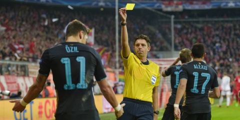 Italian Referee Gianluca Rocchi (C) shows Arsenal's German midfielder Mesut Oezil (L) the yellow card during the UEFA Champions League Group F second-leg football match between FC Bayern Munich and Arsenal FC in Munich, southern Germany, on November 4, 2015.  AFP PHOTO / GUENTER SCHIFFMANN        (Photo credit should read GUENTER SCHIFFMANN/AFP/Getty Images)