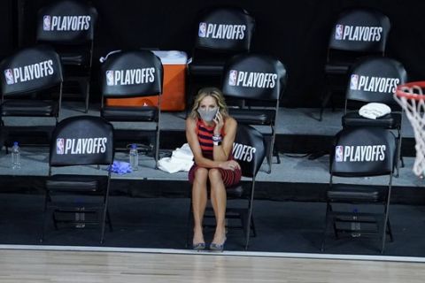 A reporter sits beside an empty court after a postponed NBA basketball first round playoff game between the Milwaukee Bucks and the Orlando Magic, Wednesday, Aug. 26, 2020, in Lake Buena Vista, Fla. The game was postponed after the Milwaukee Bucks didn't take the floor in protest against racial injustice and the shooting of Jacob Blake, a Black man, by police in Kenosha, Wisconsin. (AP Photo/Ashley Landis, Pool)