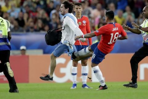 A soccer fan who intrudes onto the pitch is tackled by Chile's Gonzalo Jara (18) during a Copa America Group C soccer match between Chile and Uruguay at the Maracana stadium in Rio de Janeiro, Brazil, Monday, June 24, 2019. (AP Photo/Silvia Izquierdo)