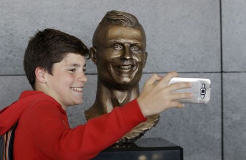 A boy takes a selfie next to the bust of Cristiano Ronaldo at the Madeira international airport outside Funchal, the capital of Madeira island, Portugal, Wednesday March 29, 2017. Madeira International Airport has been renamed after local soccer star Cristiano Ronaldo on Wednesday during a ceremony, with family, at the airport outside his Funchal hometown. (AP Photo/Armando Franca)
