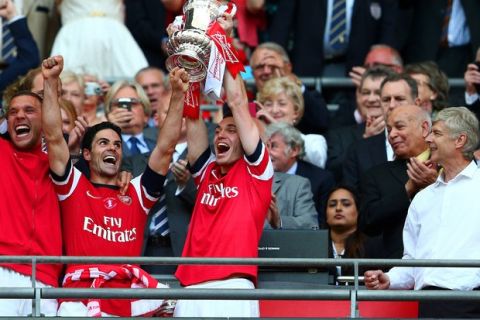 LONDON, ENGLAND - MAY 17:  Captain Thomas Vermaelen of Arsenal (2R) lifts the trophy in celebration alongside Lukas Podolski (L), Mikel Arteta (2L) and Arsene Wenger manager of Arsenal (R) after the FA Cup with Budweiser Final match between Arsenal and Hull City at Wembley Stadium on May 17, 2014 in London, England.  (Photo by Clive Mason/Getty Images)